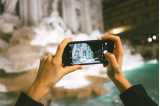 Photo: Two hands holding a mobile and photographing Fontana di Trevi in Rome.